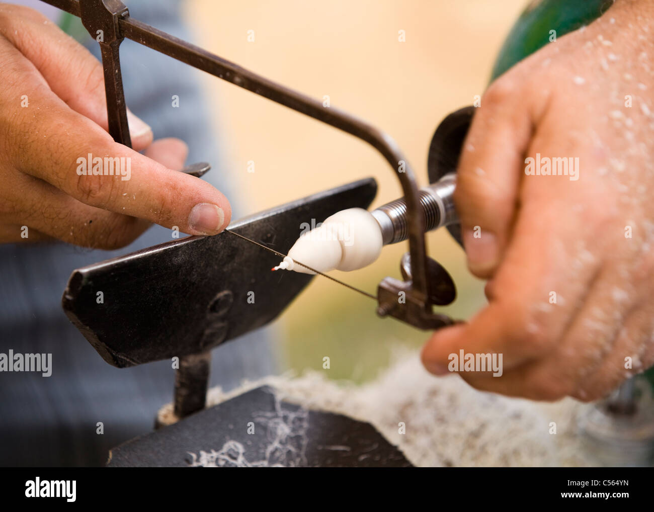 A wood carver uses a coping saw to cut a small piece of wood while turning on a lathe Stock Photo