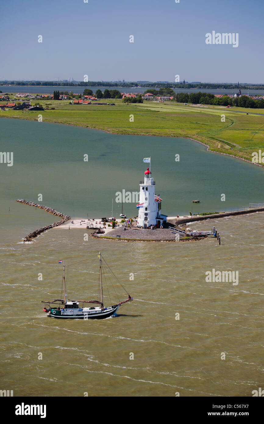 The Netherlands, Marken, traditional sailing boat passing lighthouse. Lake called IJsselmeer. Aerial. Stock Photo