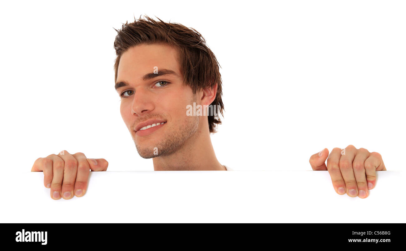 Attractive young man standing behind white wall. All on white background. Stock Photo