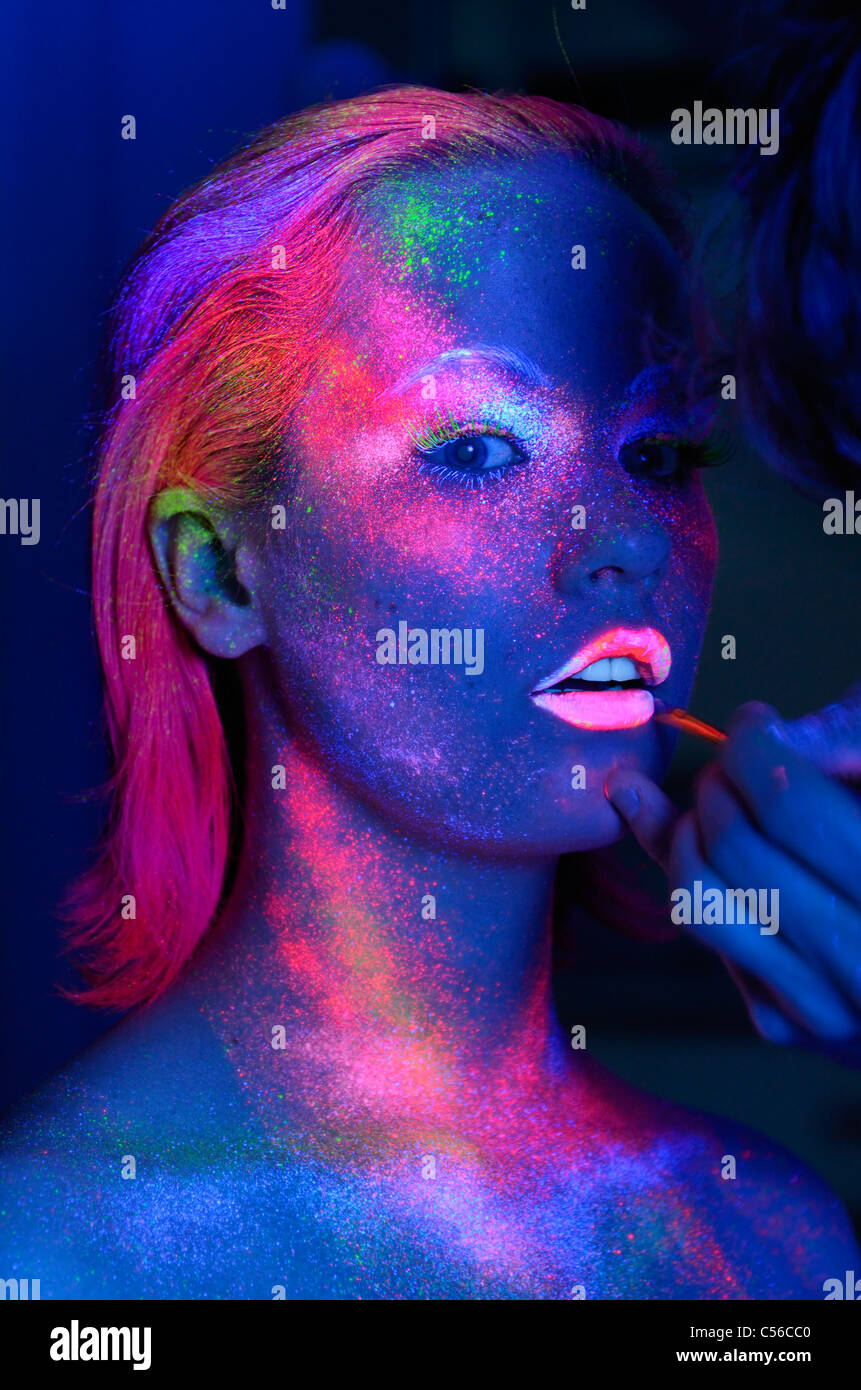 Female model getting fluorescent lipstick applied under black lights Stock Photo