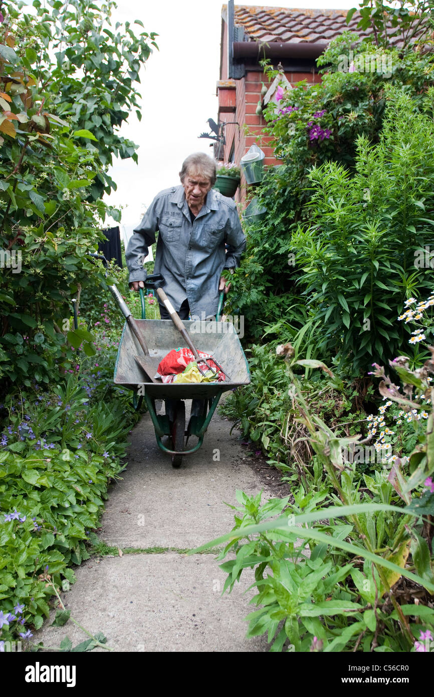 gardening man pushing a wheelbarrow up a flower garden path Stock Photo