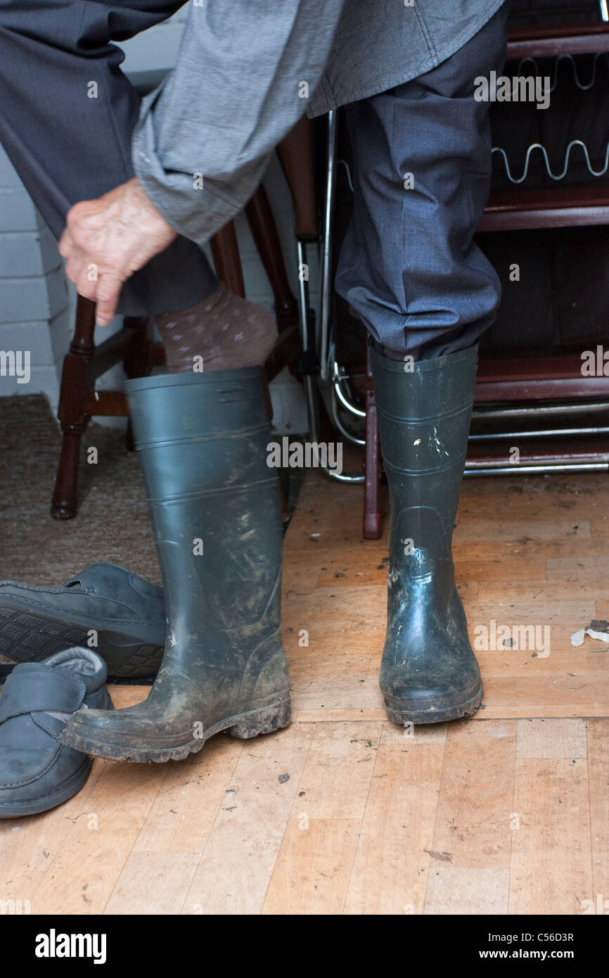 man in old garden shed putting feet in old wellington boots ready for gardening Stock Photo