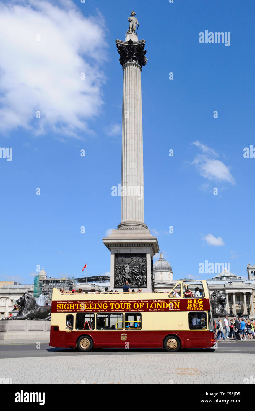 London street scene tourists on double decker open top sightseeing tour bus passing Nelsons Column in Trafalgar Square England UK  blue sky summer day Stock Photo