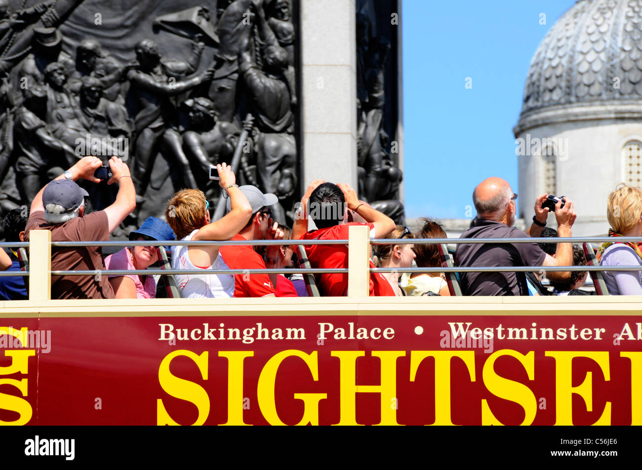 Tourists on open top bus taking pictures of Nelsons column and Trafalgar Square Stock Photo