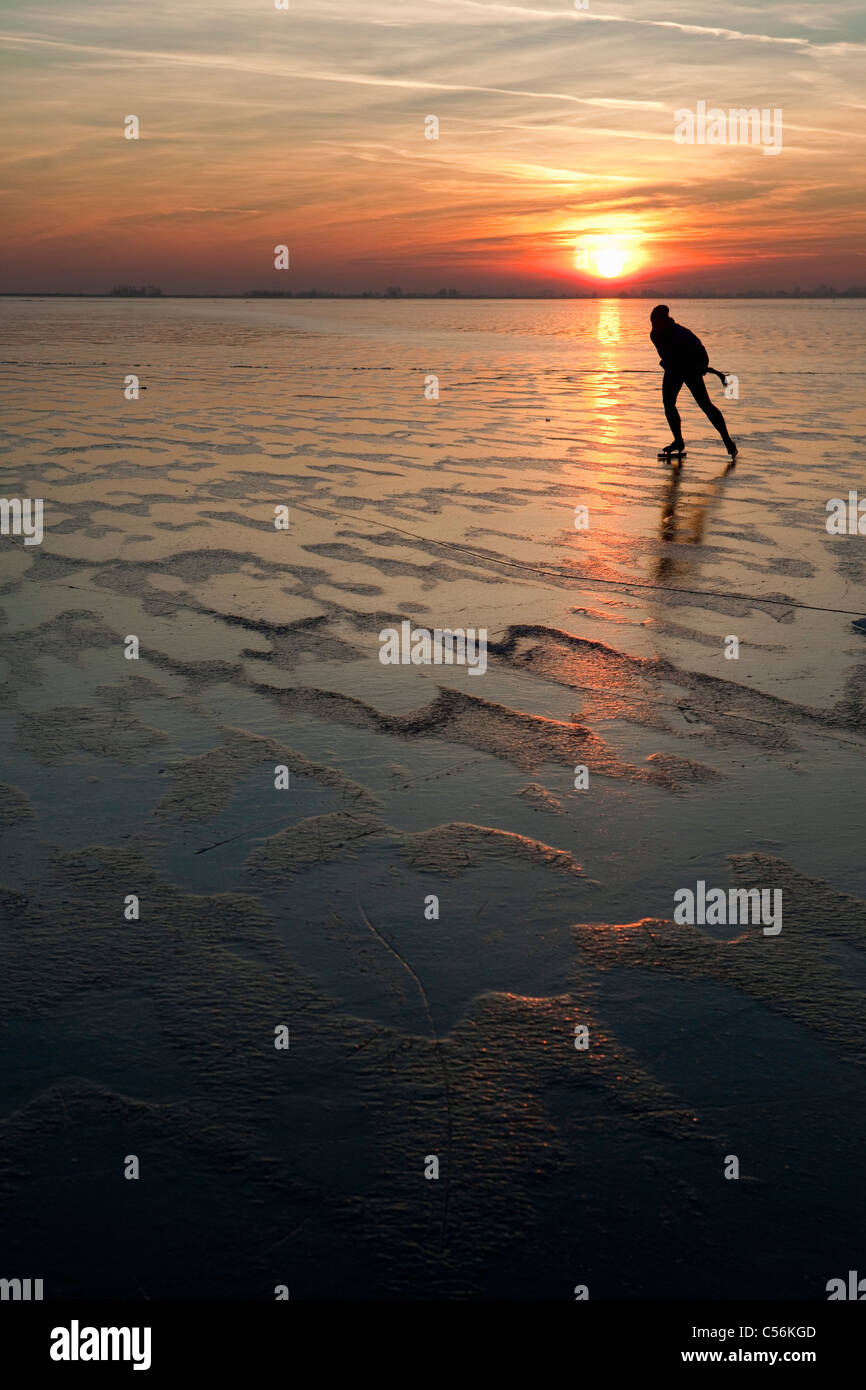 The Netherlands, Marken, Frozen lake called IJsselmeer. Sunset. Man ice skating. Stock Photo