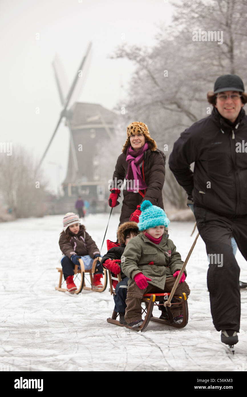 The Netherlands, Ankeveen. Family ice skating and sledging in front of windmill. Stock Photo