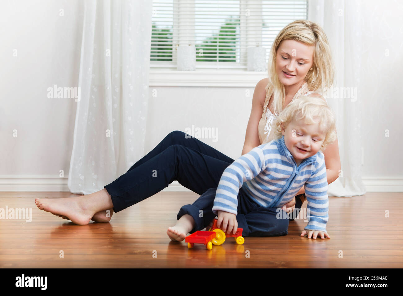 Smiling young mother sitting with child playing on floor Stock Photo ...