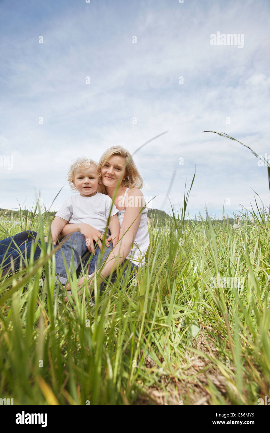 Portrait Of Mother Sitting On Grass With Her Son Against Cloudy Sky