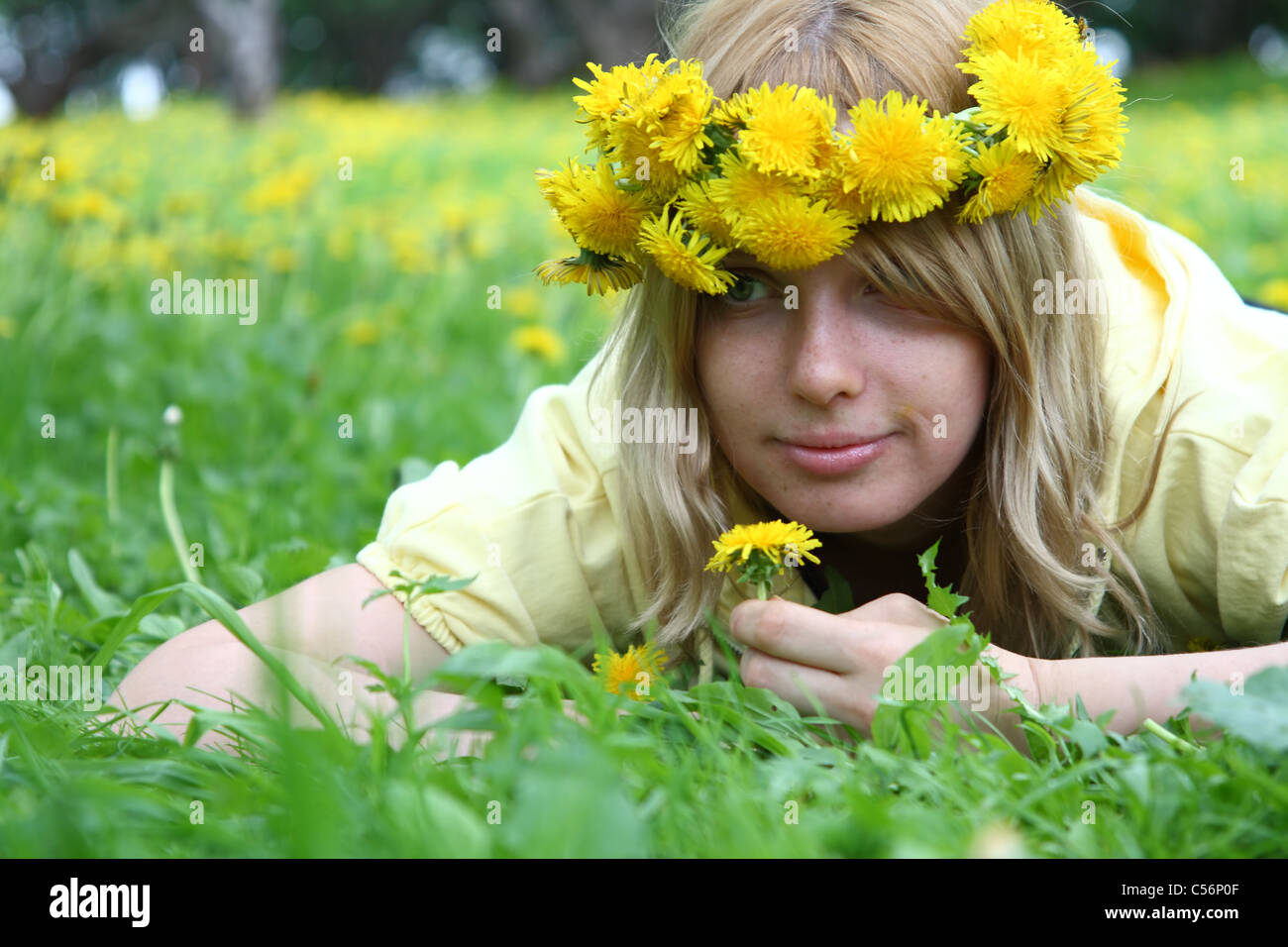 cheerful young woman with dandelion wreath on her head lying down on the green grass Stock Photo
