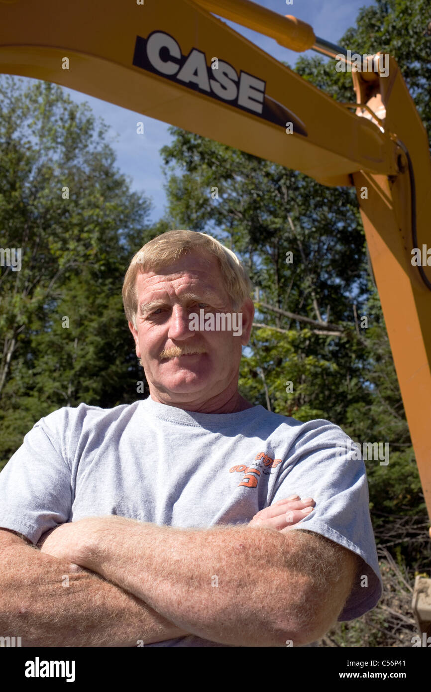 Backhoe driver stands proudly under the arm of his machine Stock Photo