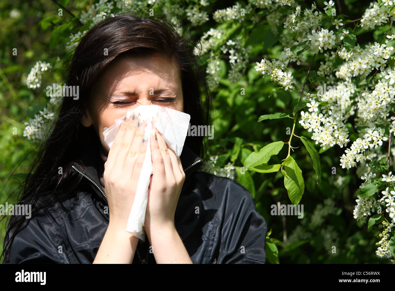 allergy to pollen: young woman blowing nose among flowers Stock Photo