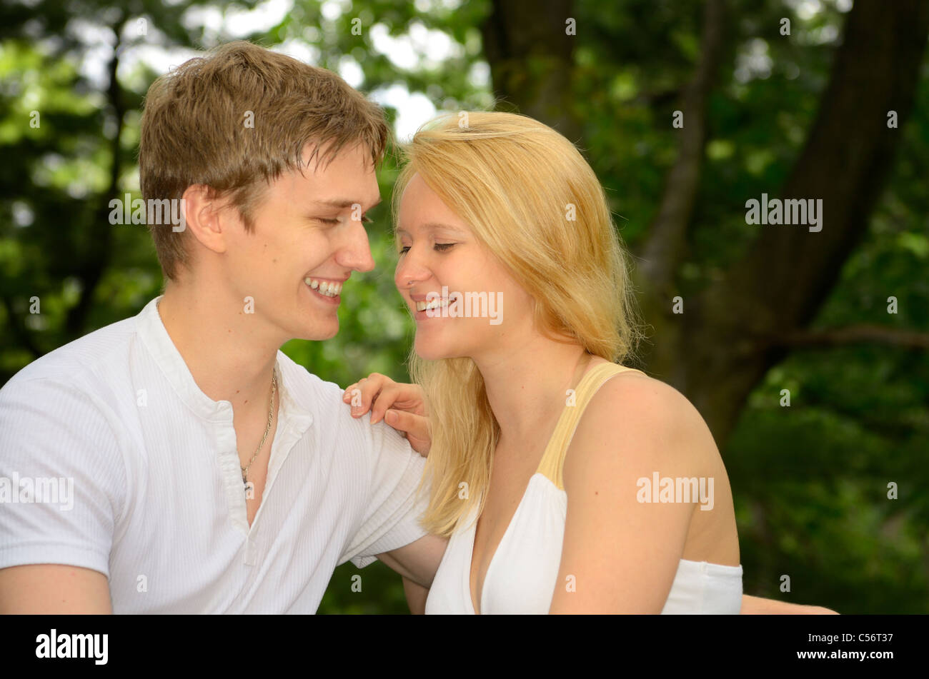 Male and female fair haired lovers touching and laughing while sitting on a park bench Stock Photo