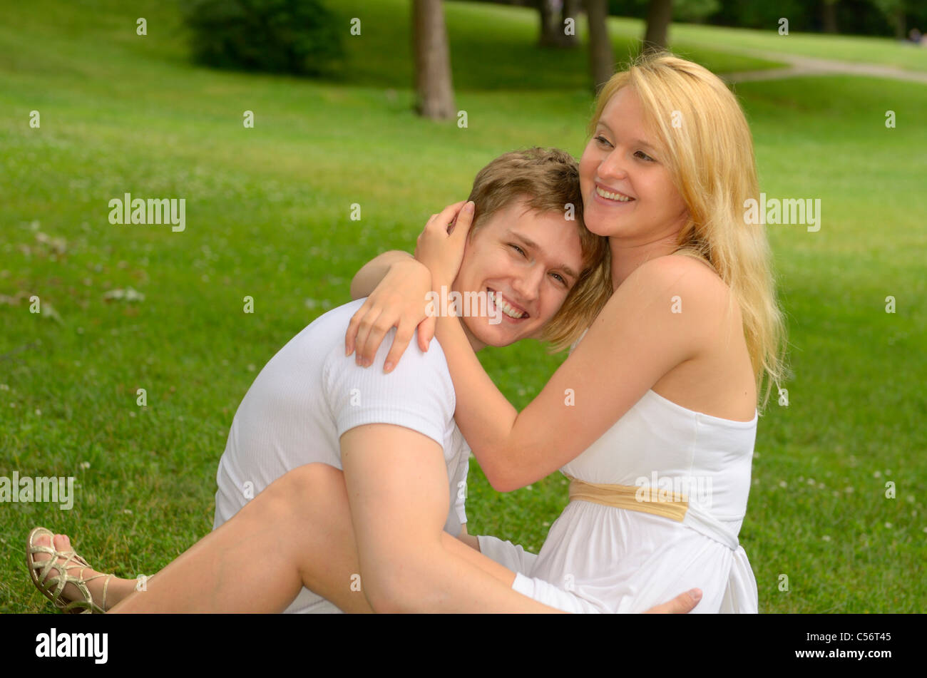 Happy smiling white couple embracing while lounging on a field of grass in a park Stock Photo