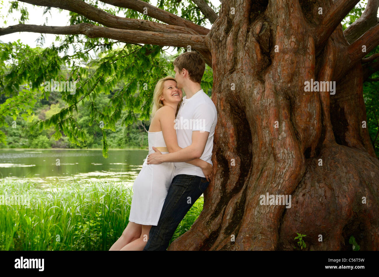 Happy couple embracing under a large Dawn Redwood tree on the shore of a lake Grenadier Pond High Park Toronto Stock Photo