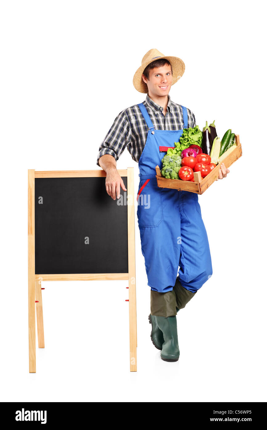 A farmer holding a crate full with vegetables and posing next to an ...