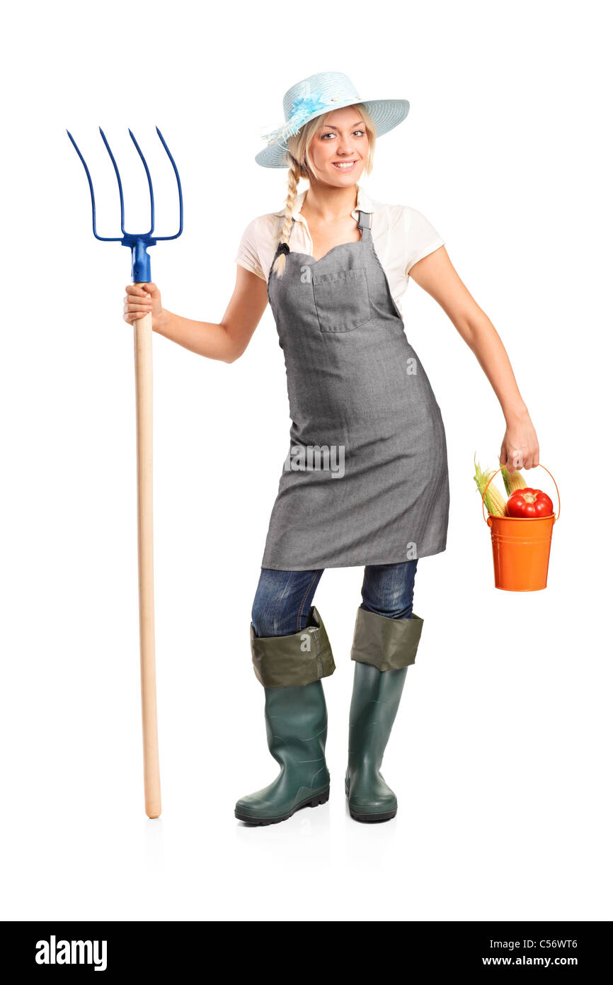 Full length portrait of a female farmer holding a pitchfork and bucket with vegetables Stock Photo