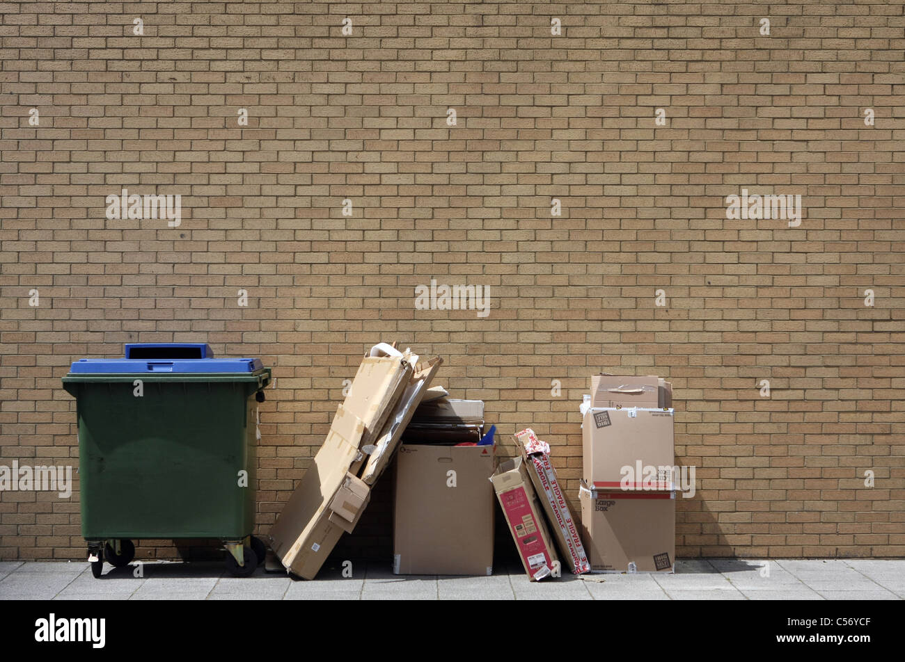 Pile of waste cardboard next to a green wheelie bin Stock Photo