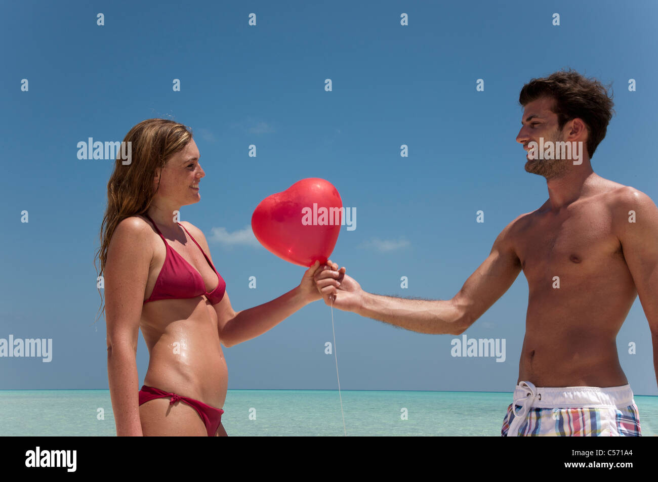 Couple sharing red balloon on beach Stock Photo