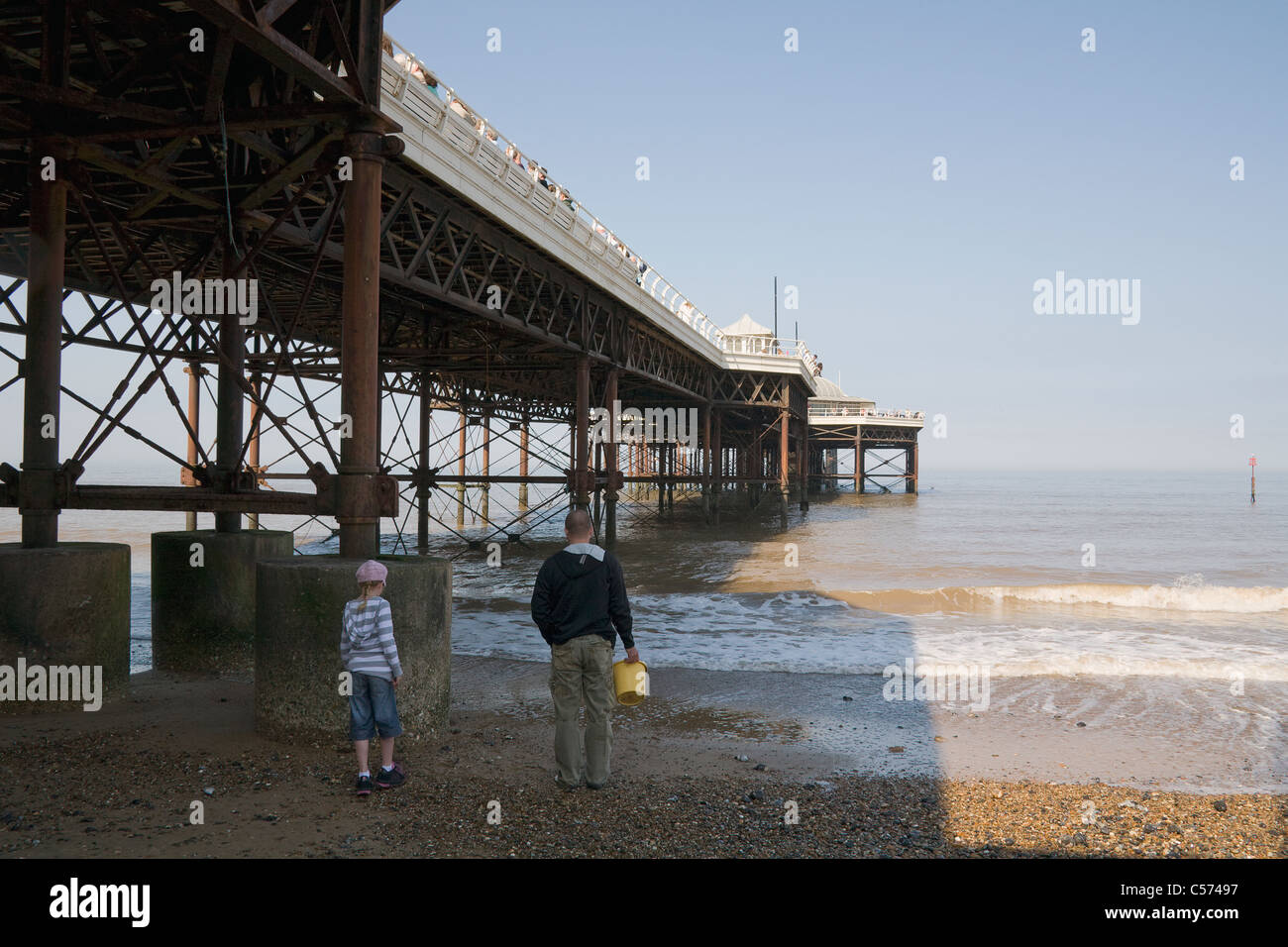A young lad with adult, walking down to the shore to join others trying to catch crabs under Cromer pier. Stock Photo