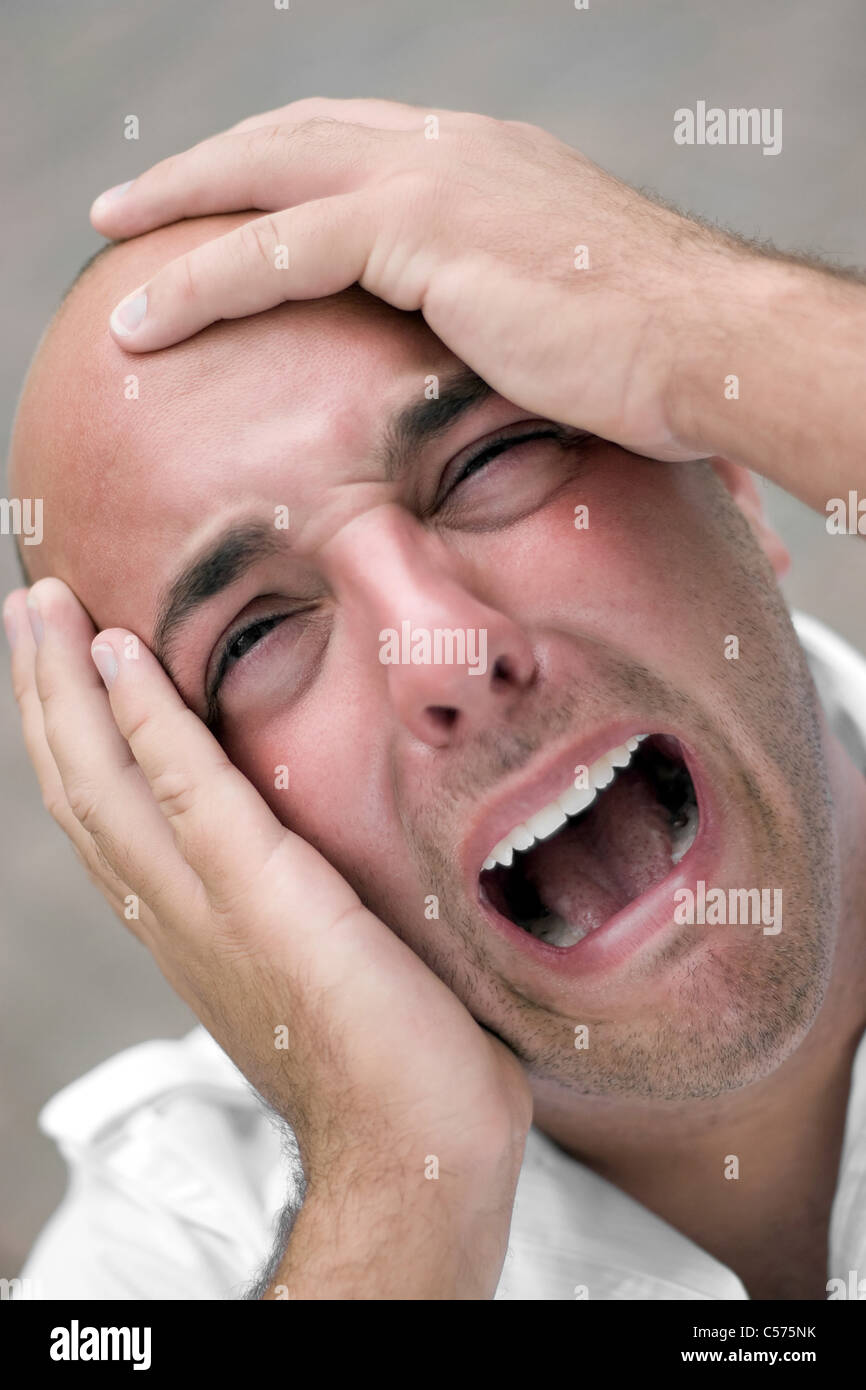 A man that looks distraught and mentally overloaded grabs his bald head in agony and desperation. Shallow depth of field. Stock Photo