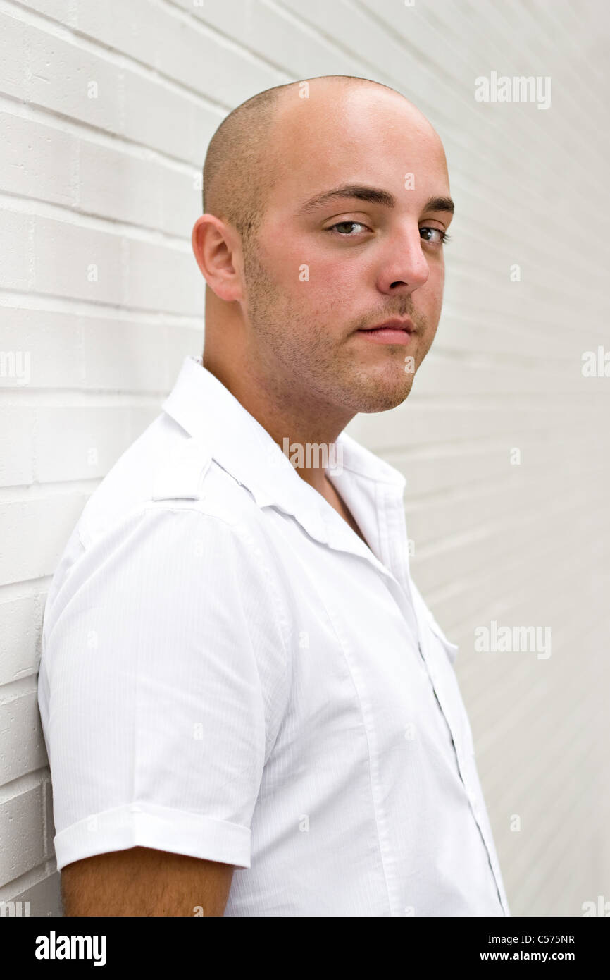 Portrait of a young man in the city standing in front of a white brick ...