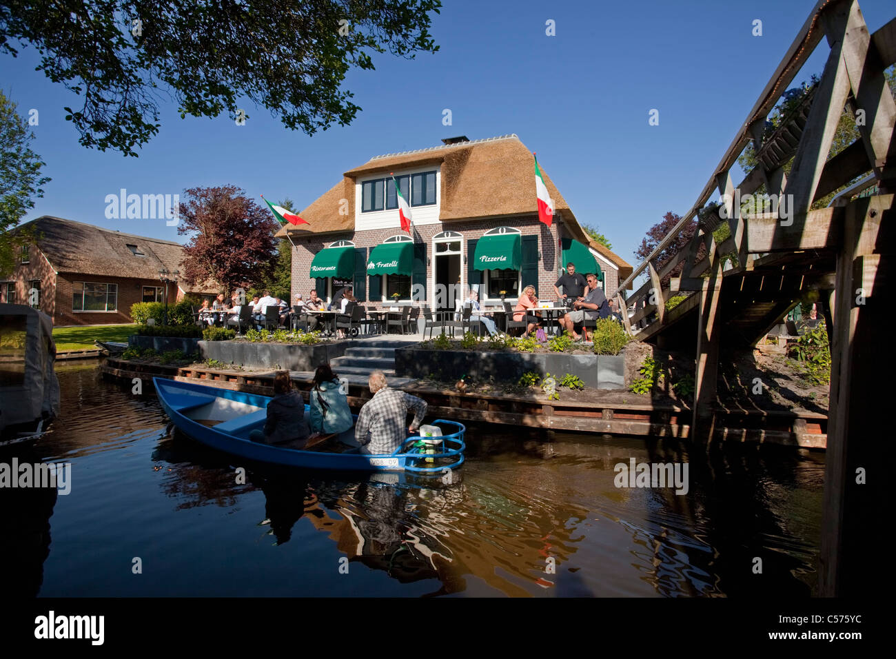 The Netherlands, Giethoorn, Village with almost only waterways. Italian restaurant and outdoor cafe. Boat pasing. Stock Photo