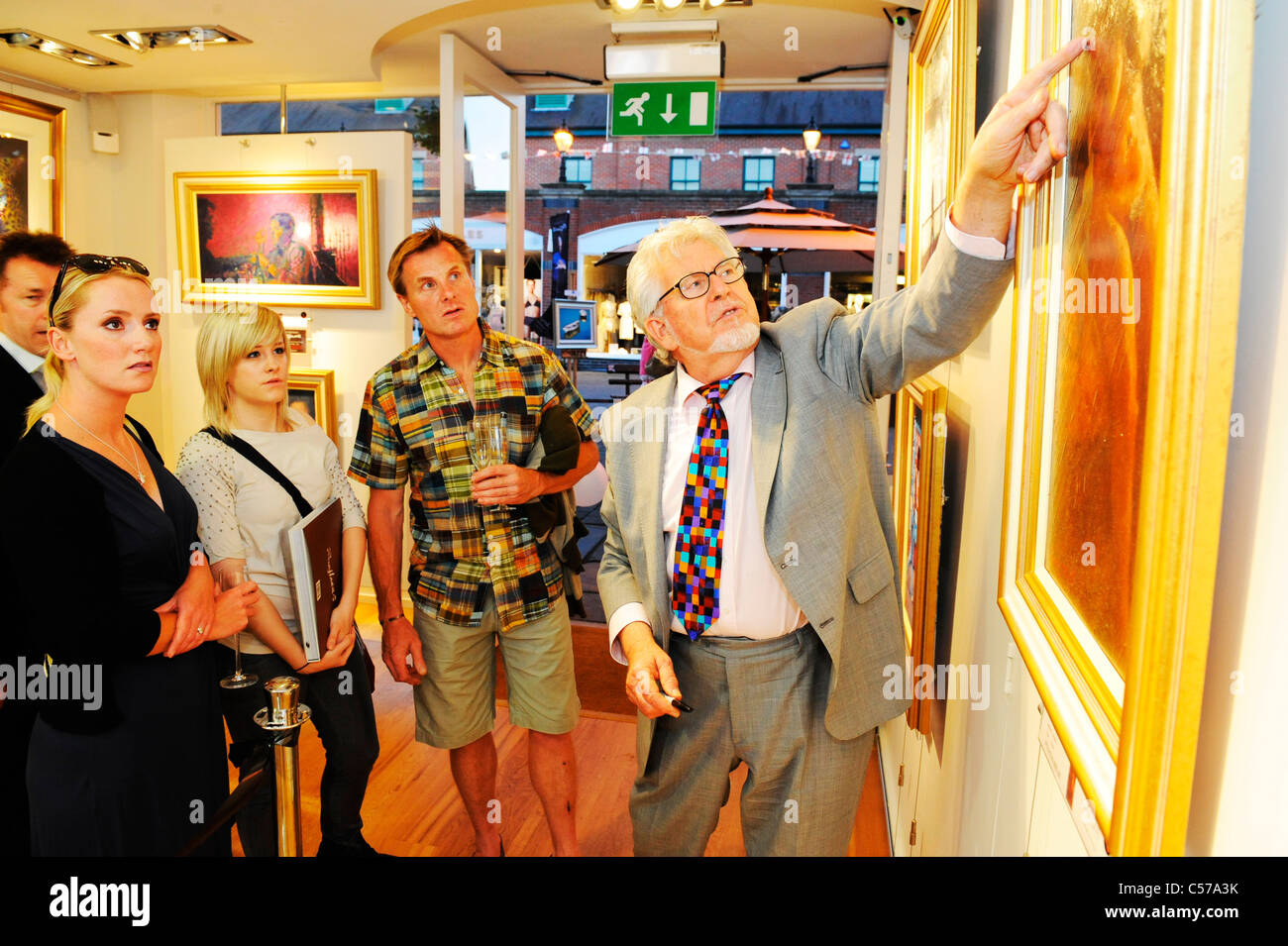 rolf harris talks through one of his paintings with members of the