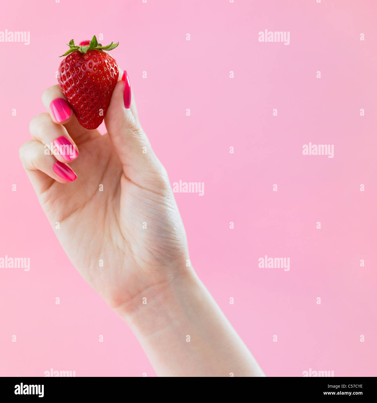 pink colored nail hand grab the strawberry Stock Photo