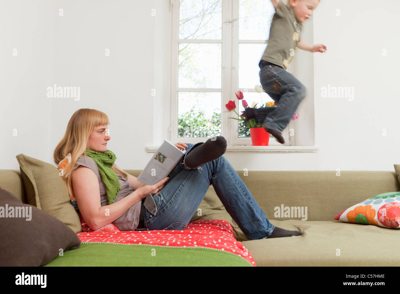 Mother relaxing as son jumps on sofa Stock Photo