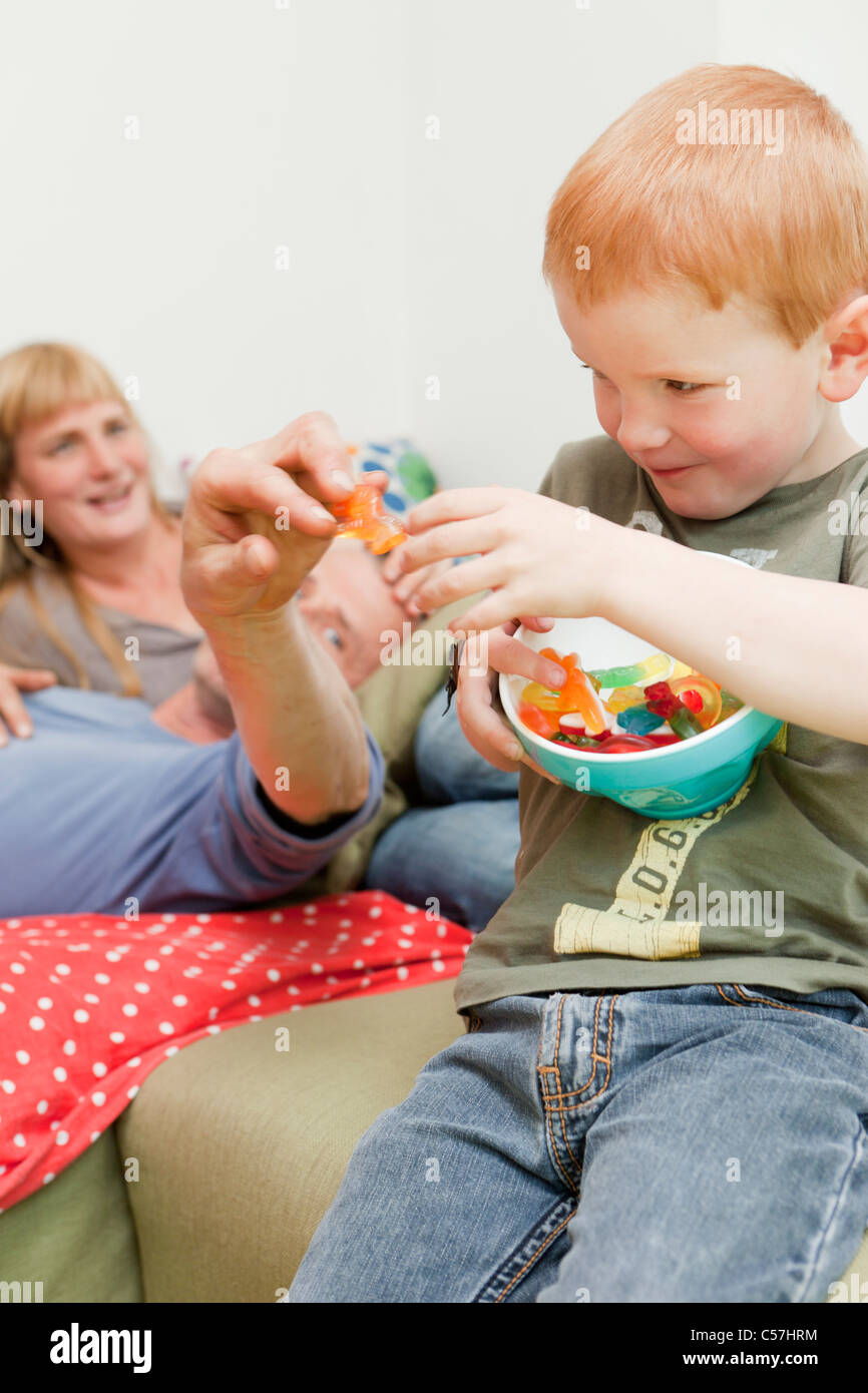 Son sharing candies with father on sofa Stock Photo