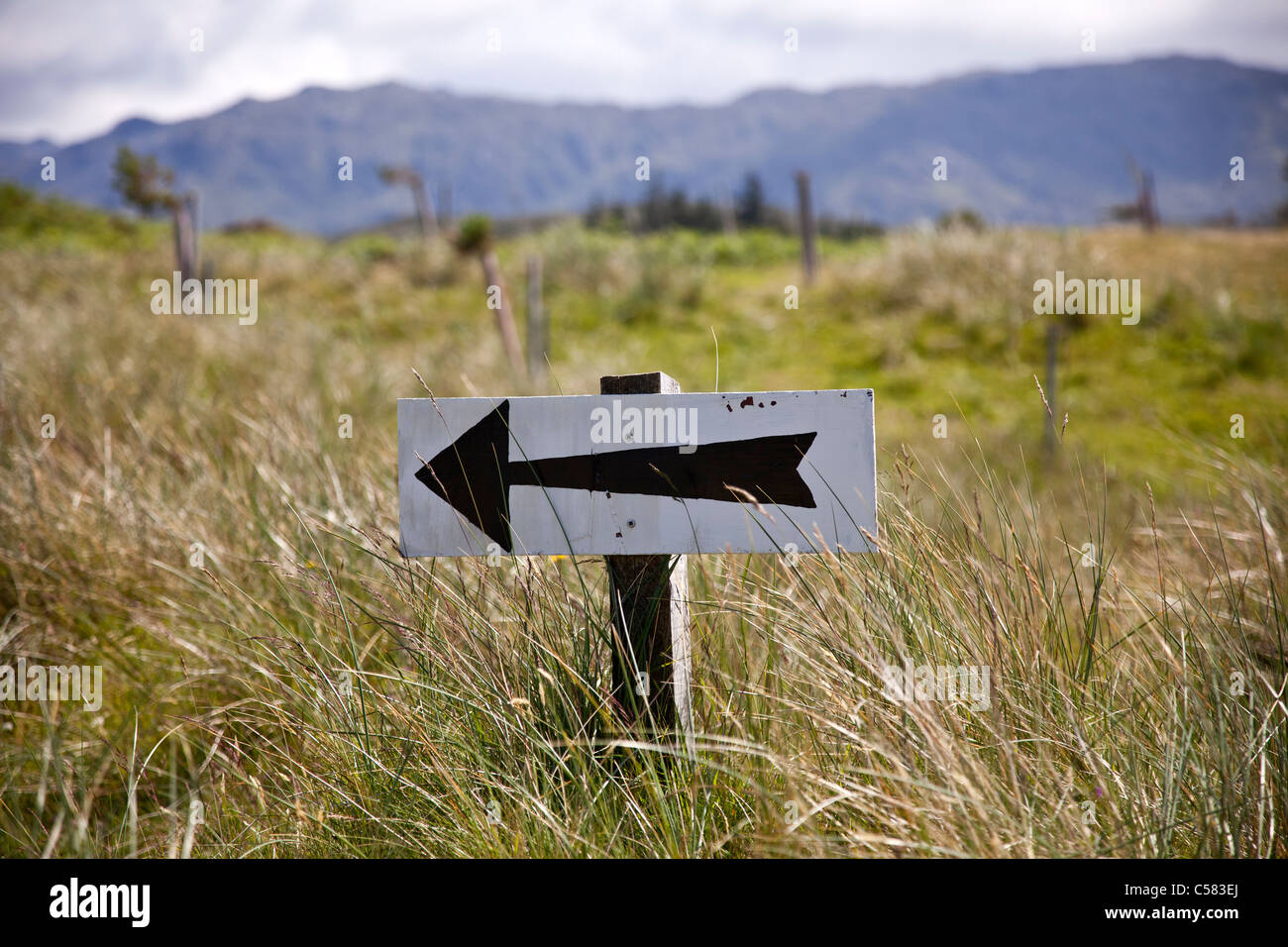 A black painted arrow pointing left in the middle of a field against the back drop of mountains in the West of Scotland. Stock Photo