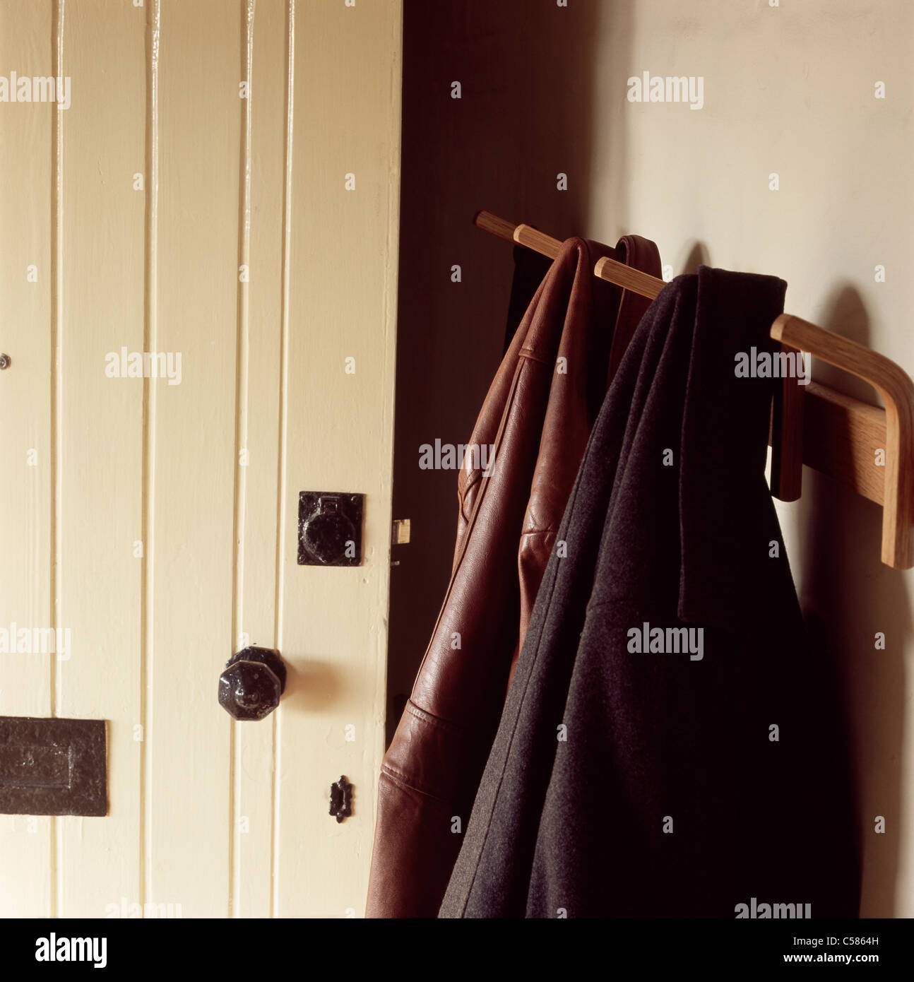 Coats hanging on a coat peg by a wooden painted front door Stock Photo