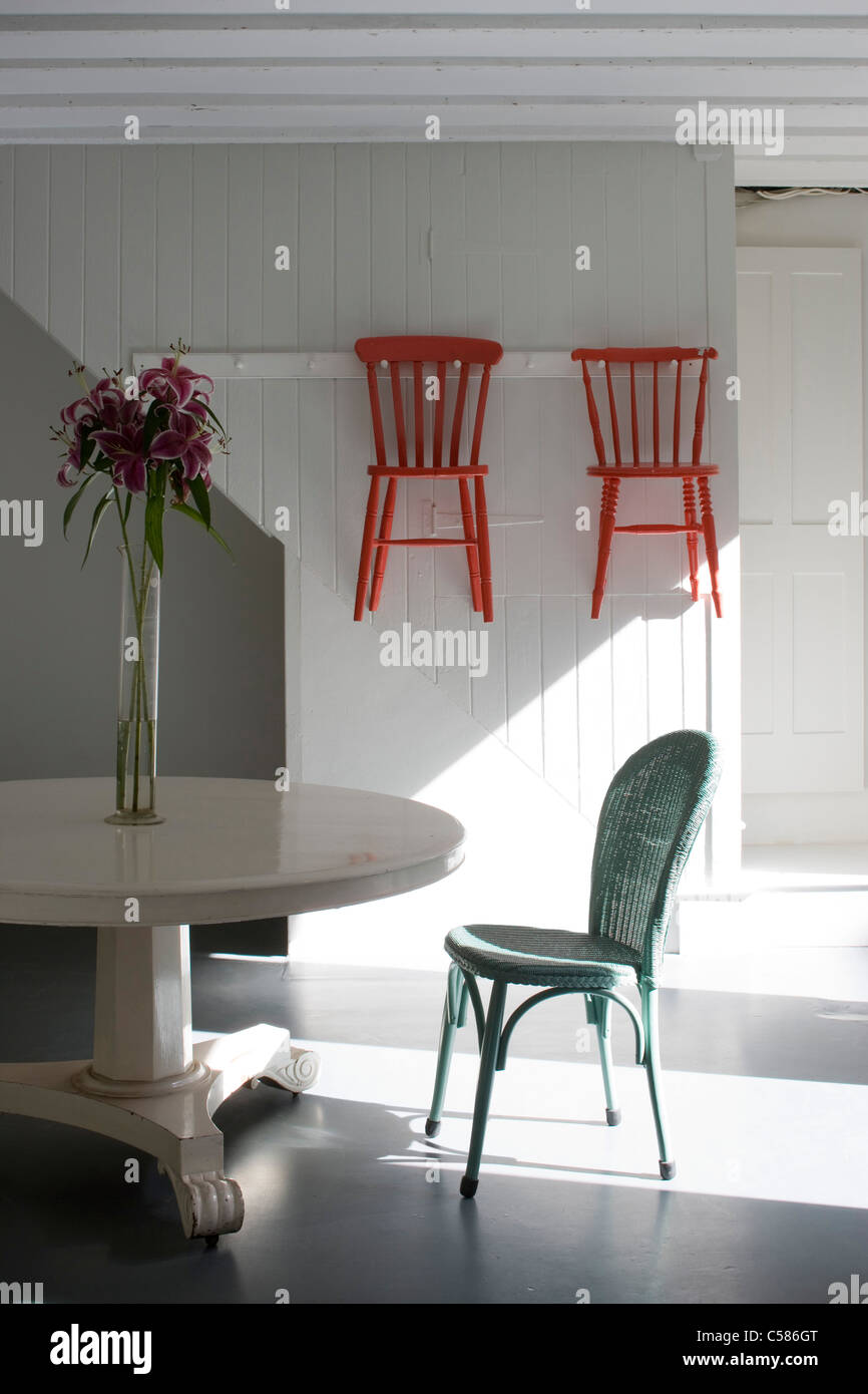 Kitchen with white painted pedestal table, Lloyd Loom chair and shaker style hanging chairs. Stock Photo