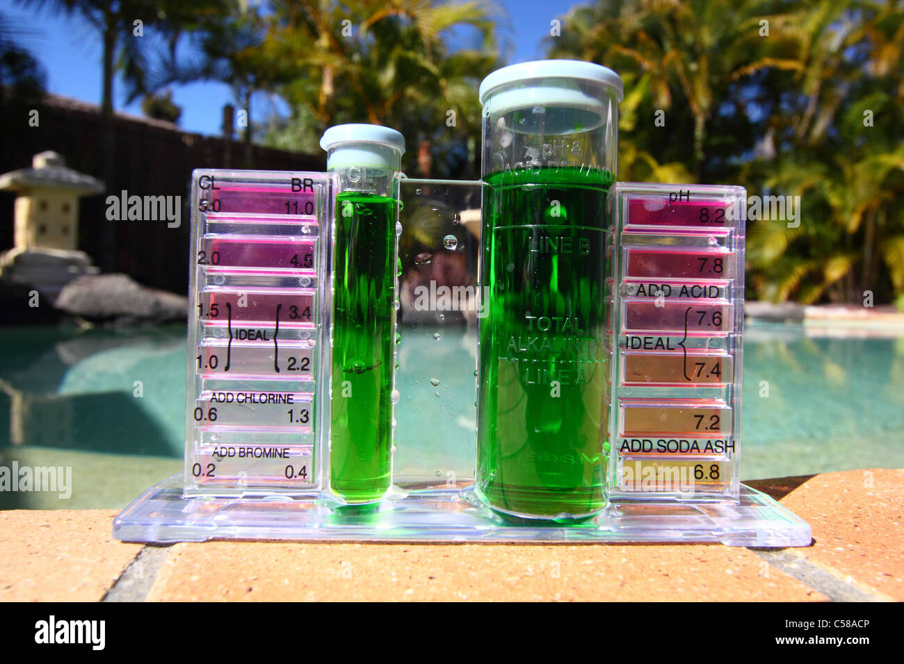 SAMPLE OF SLIMY GREEN WATER IN A POOL TEST KIT BLUE SKY AND POOLSIDE BACKGROUND HORIZONTAL BDB