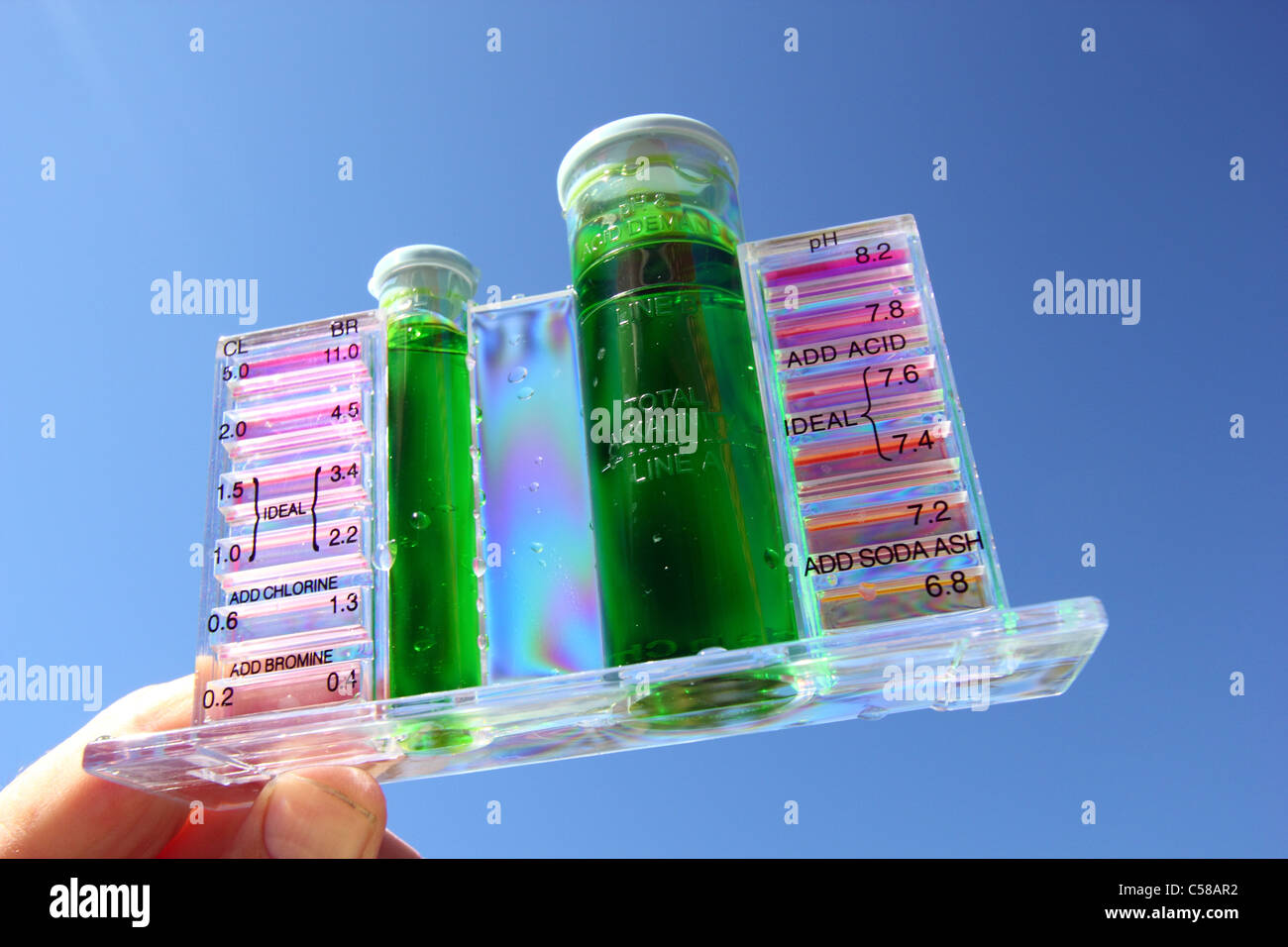 SAMPLE OF SLIMY GREEN WATER IN A POOL TEST KIT BLUE SKY AND POOLSIDE BACKGROUND HORIZONTAL BDB
