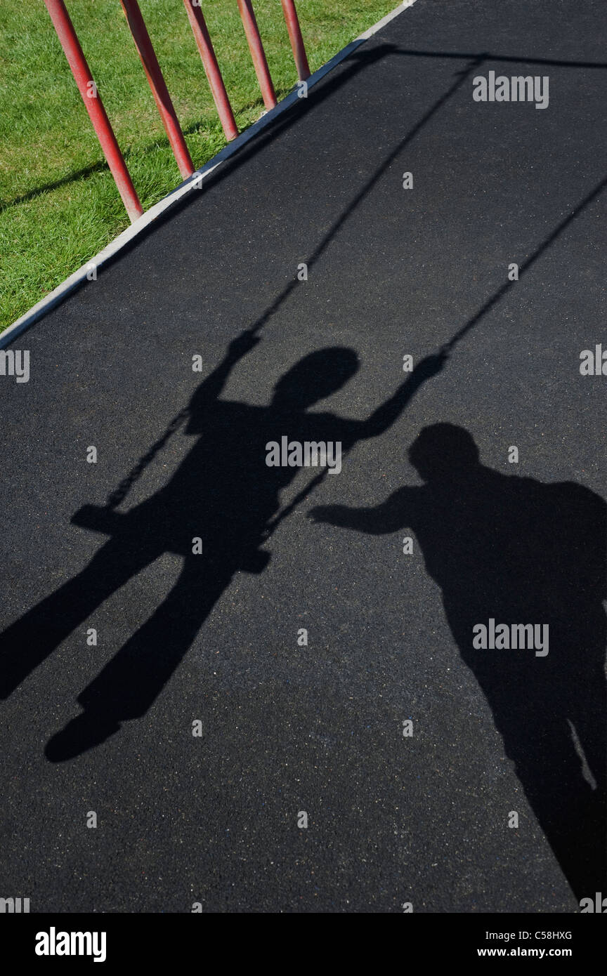 Social Distancing Isolation Child Abuse concept. Menacing Shadow of a man looming over a child playing on a swing in a children's playground Stock Photo