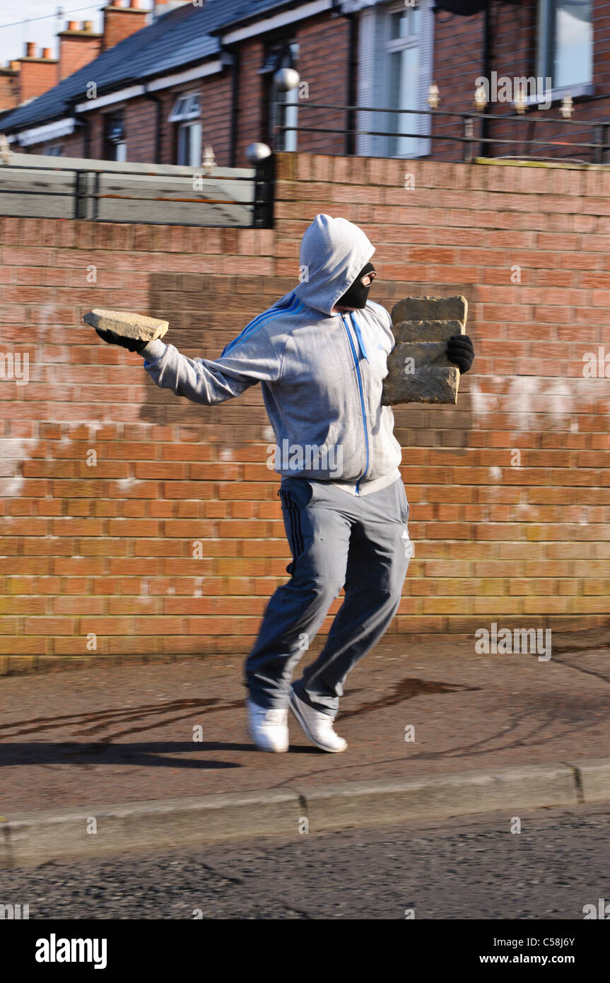 Masked rioter throws brick at police riot control line Stock Photo