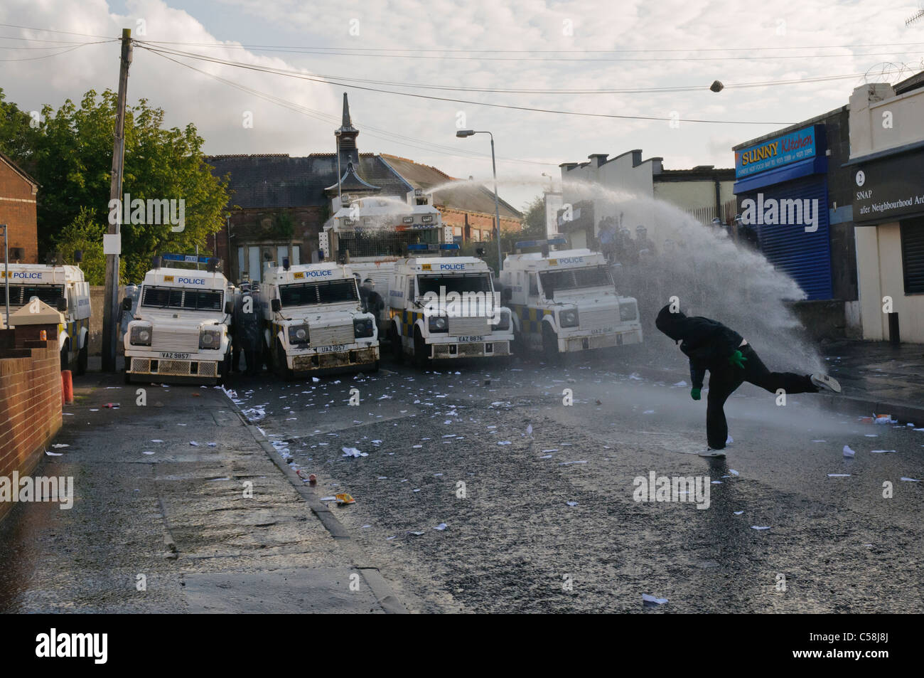 Rioter throws brick at police, while water cannon targets him Stock Photo