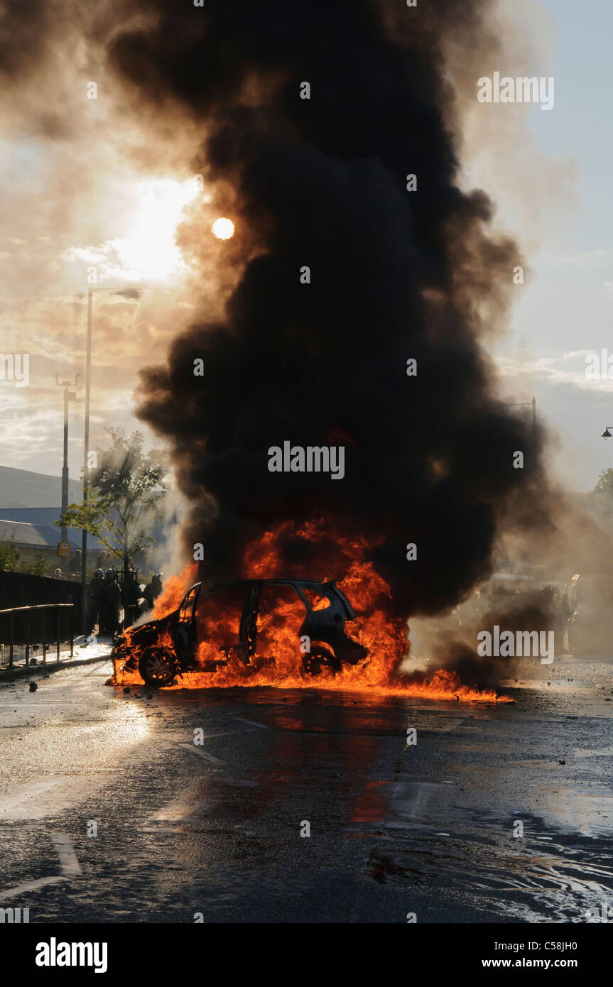 A car burning in the middle of a road, with lots of black smoke Stock Photo