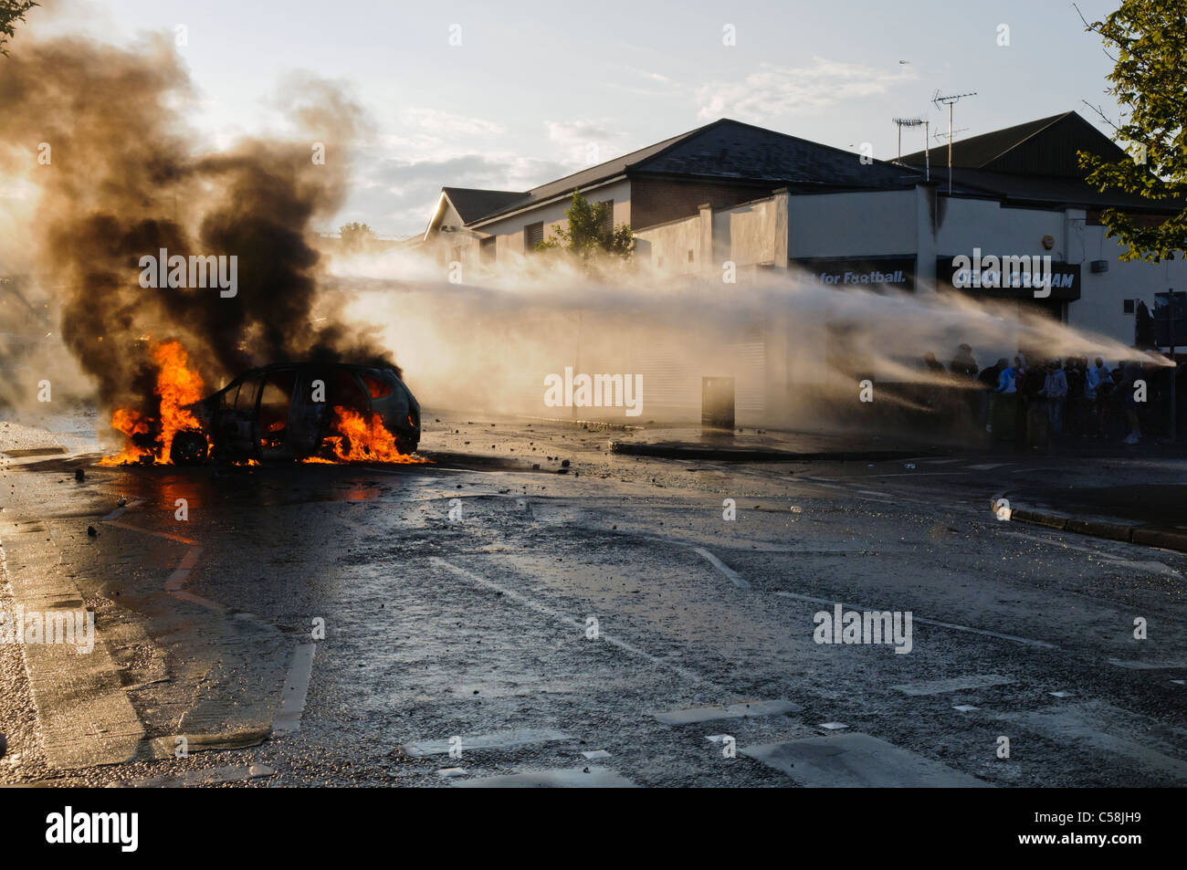 Rioters set fire to a stolen car while water cannon disperse rioters Stock Photo