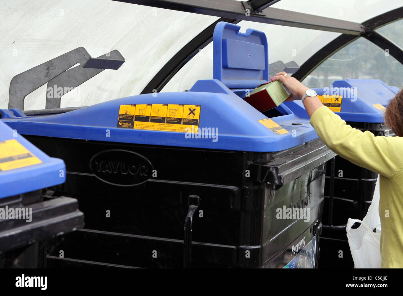 A lady putting rubbish in one of a row of wheelie bins in a car park in