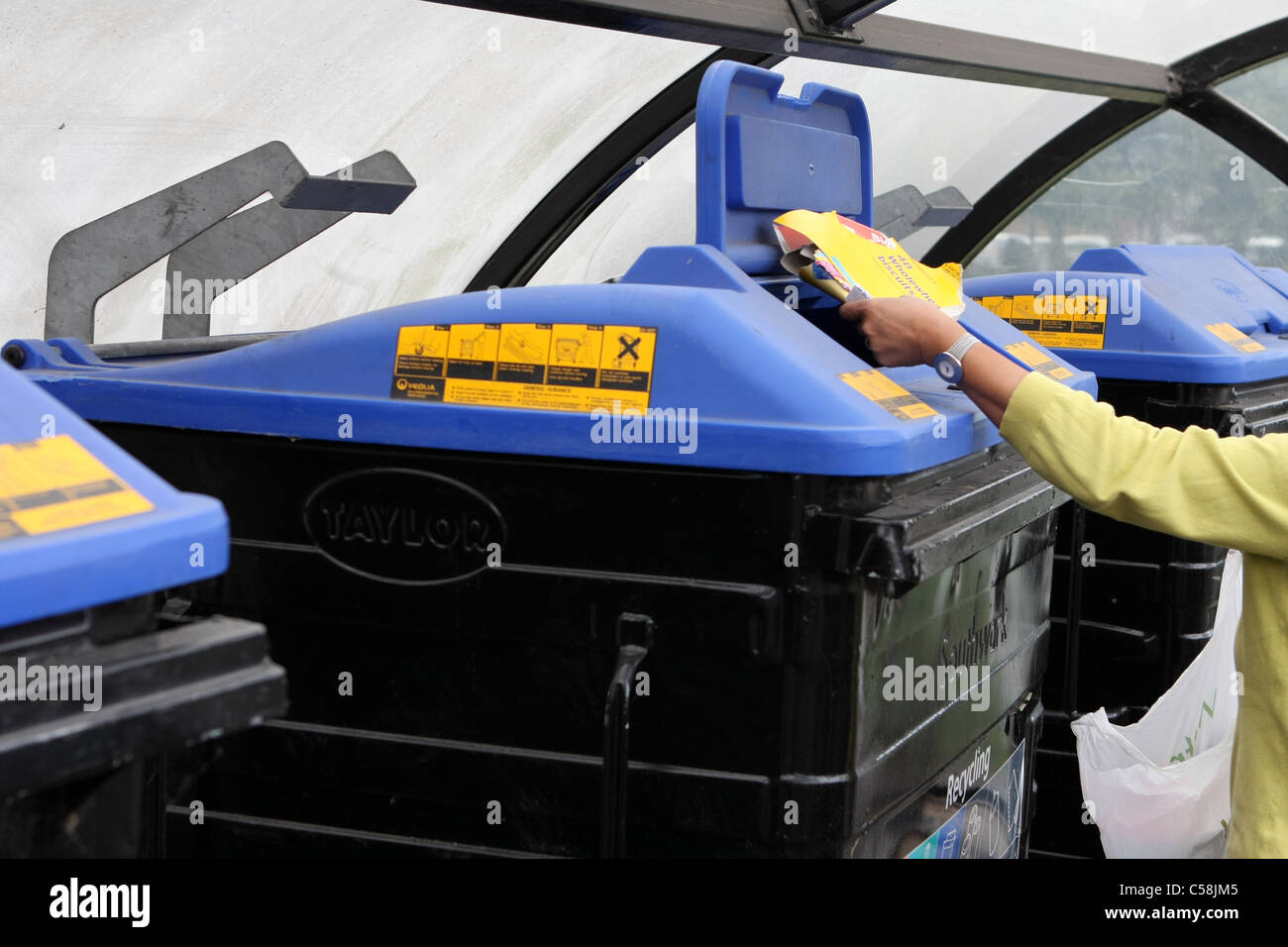 A lady putting rubbish in one of a row of wheelie bins in a car park in