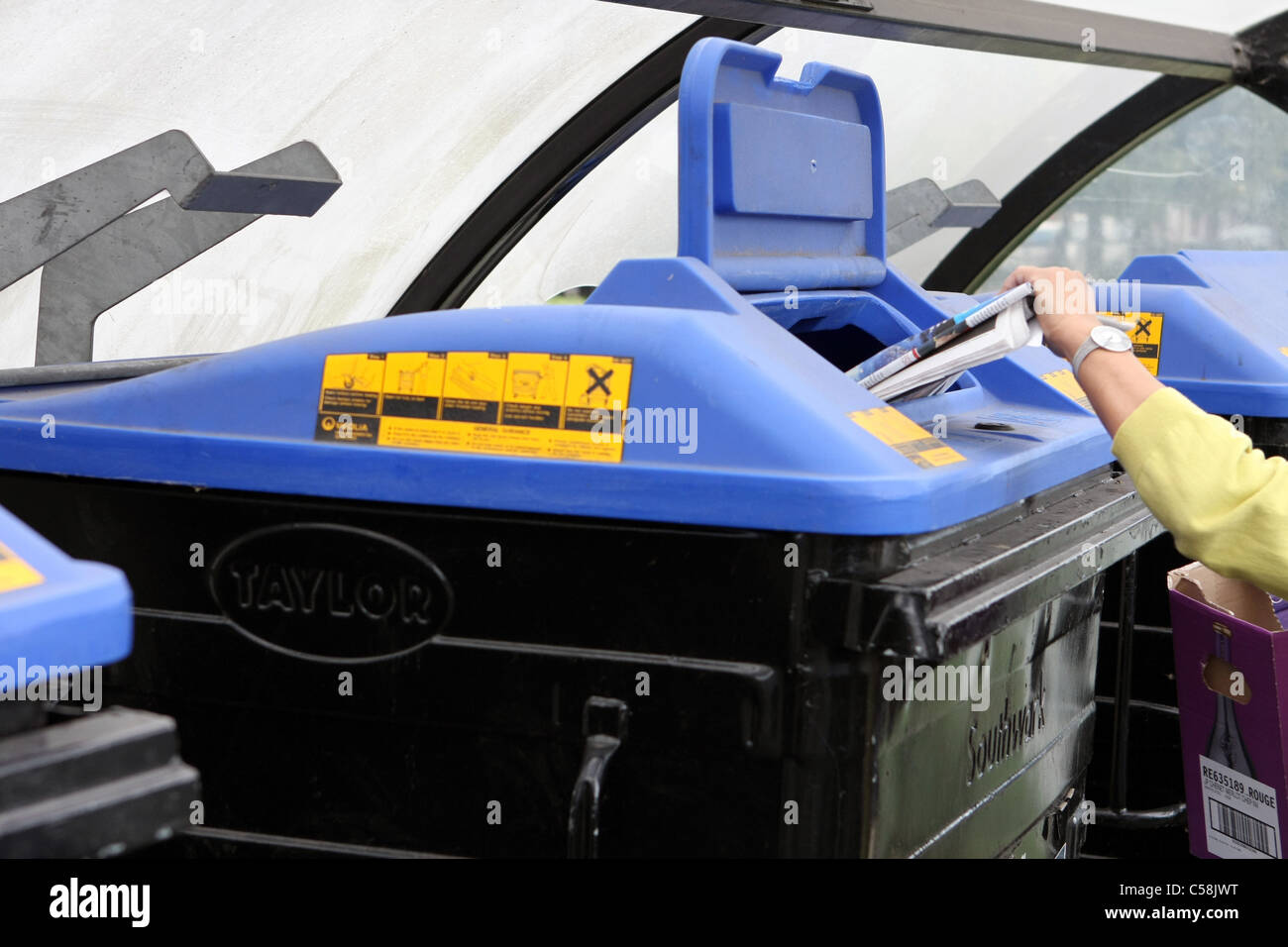 A lady putting rubbish in one of a row of wheelie bins in a car park in