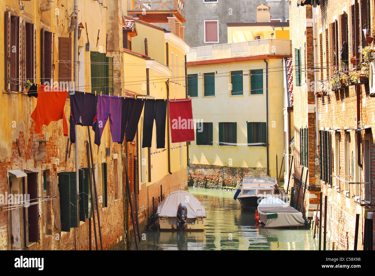 Small canal with boats among old brick houses with washed clothes in Venice, Italy. Stock Photo