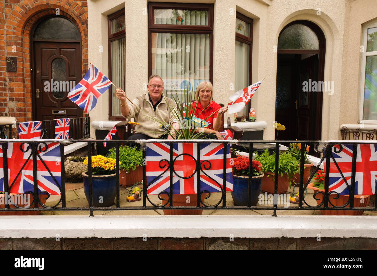 Two people waving flags in a garden decorated with Union Jacks at a street party Stock Photo