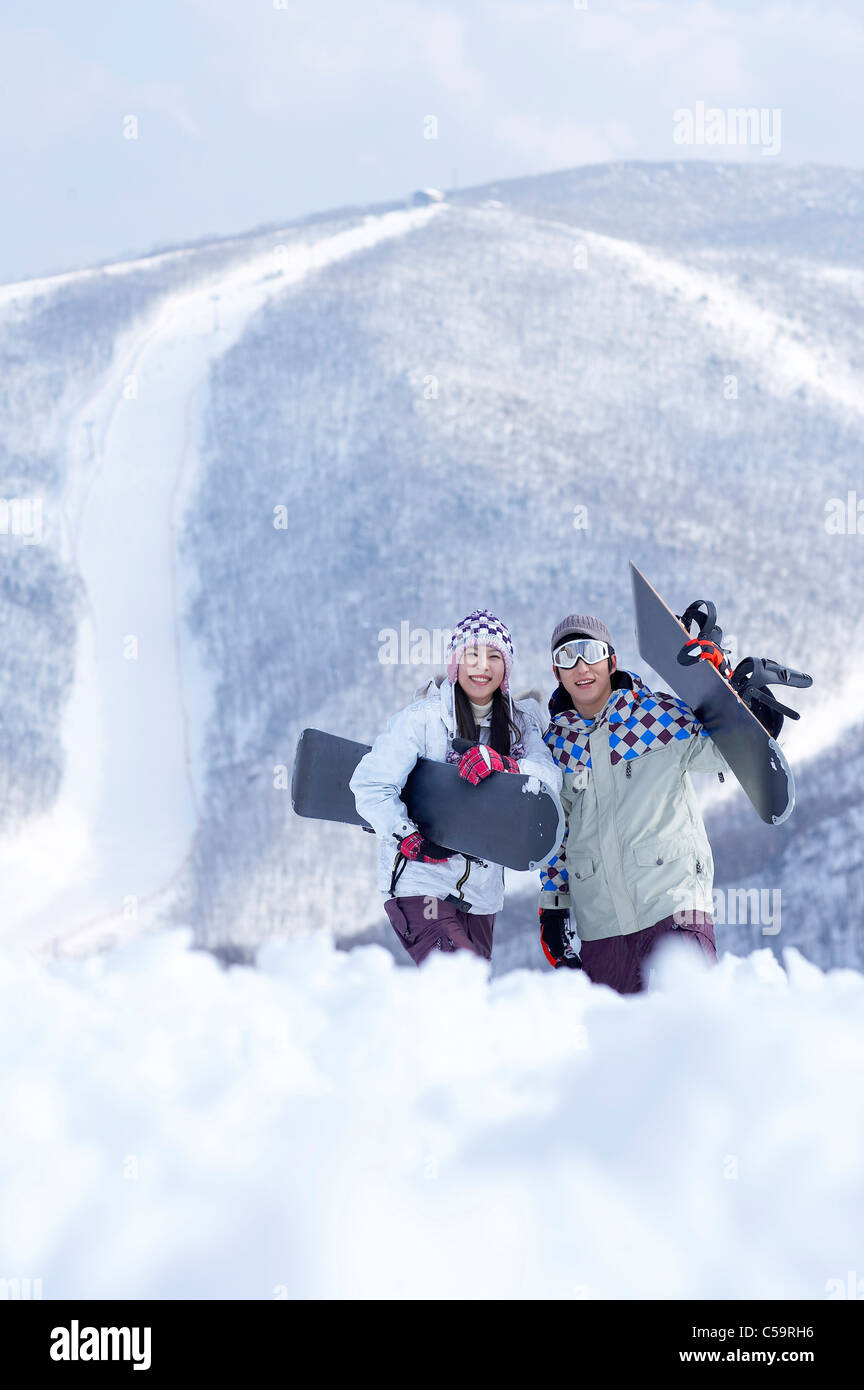 Portrait of young man and woman standing on snowcapped land, holding ...