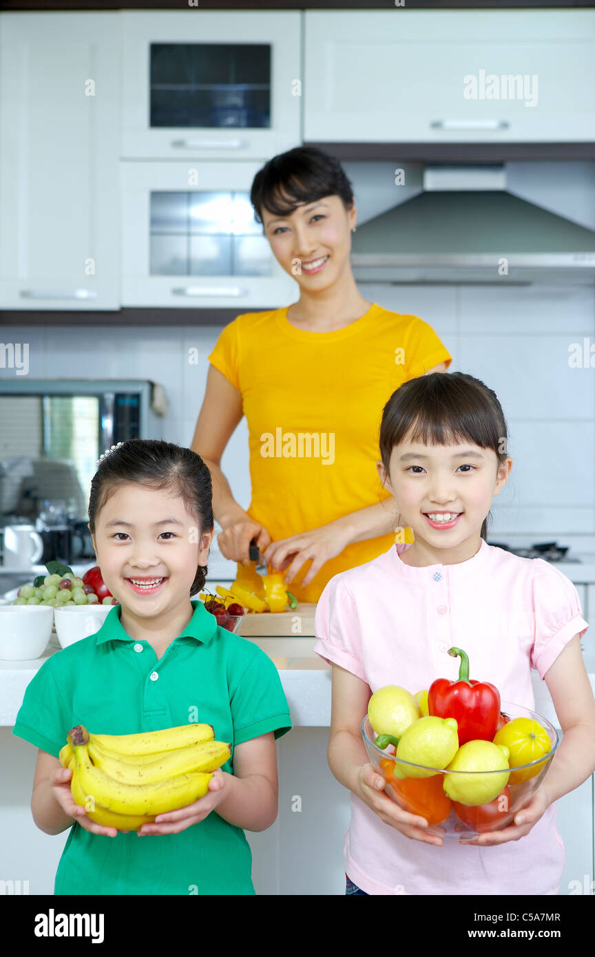 Portrait of daughters holding bowl of vegetables and bananas, while mother standing in background Stock Photo