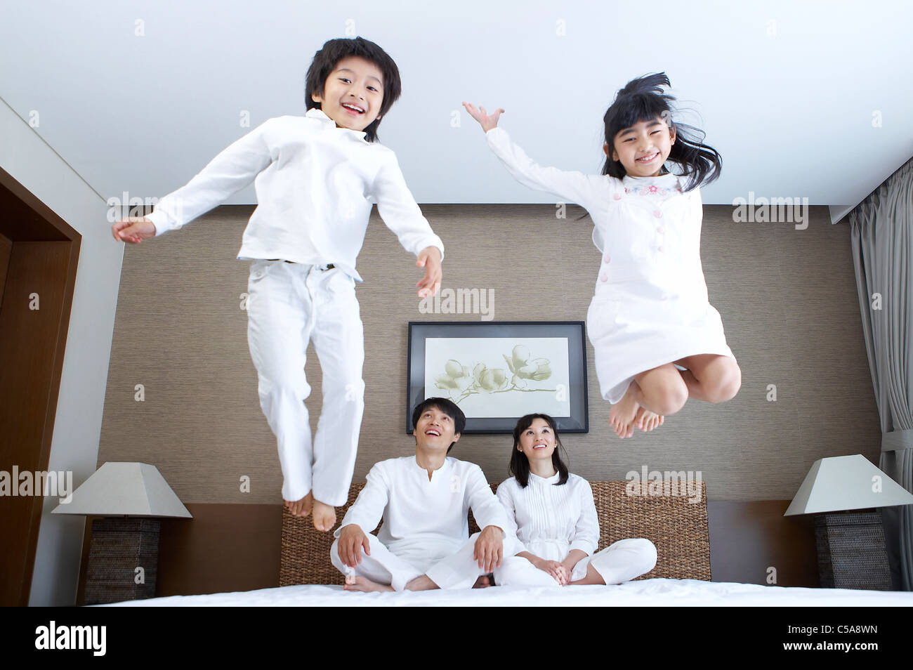 Portrait of children jumping on bed, while parents looking Stock Photo