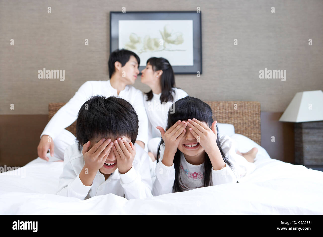 Close-up of children covering eyes, while parents kissing in background Stock Photo