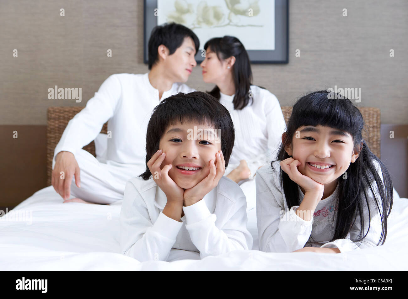 Close-up of children smiling, while parents kissing in background Stock Photo
